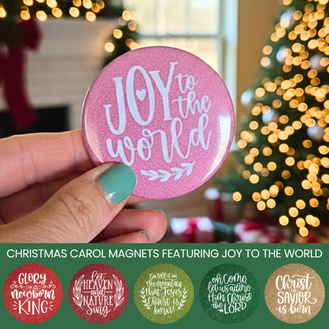 Pink magnet with 'Joy to the World' text held by a hand, Christmas tree in the background