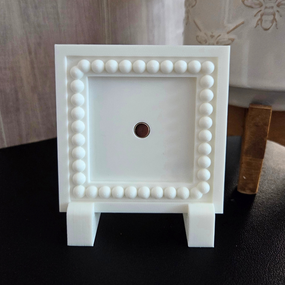 White 3D‑printed square magnetic frame with decorative beaded border, holding one photo magnet, displayed on a tabletop with removable feet.