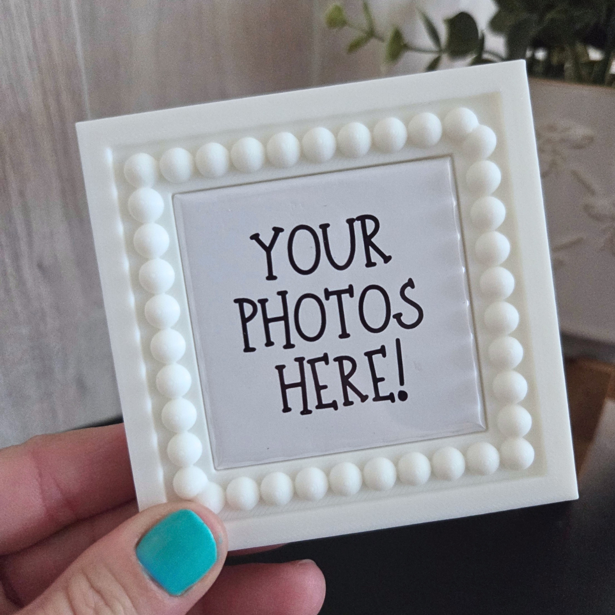 Small white magnetic frame with 'Your Photos Here!' text held by a hand