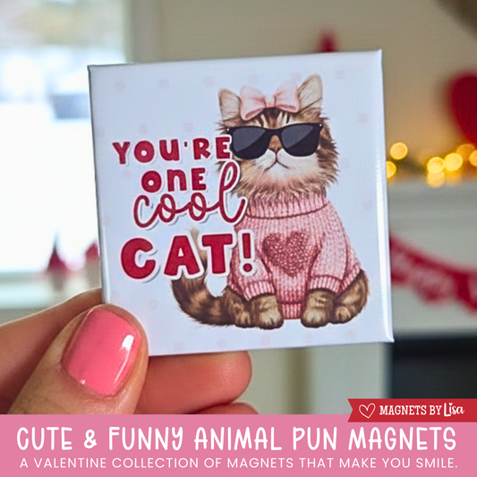 A valentine's day themed magnet that features a cat with text that reads "You're one cool cat!" in the colors or red and pink.  THe cat is wearting sunglasses and a pink sweater with a heart in the middle.  and a pink bow in it's head. 