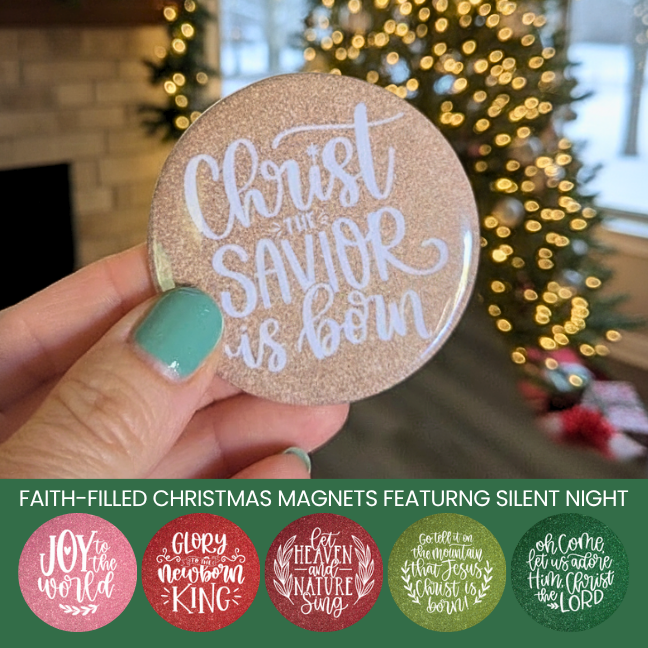 Hand holding a Christmas magnet with 'Christ is the Savior is Born' text, blurred Christmas tree in the background