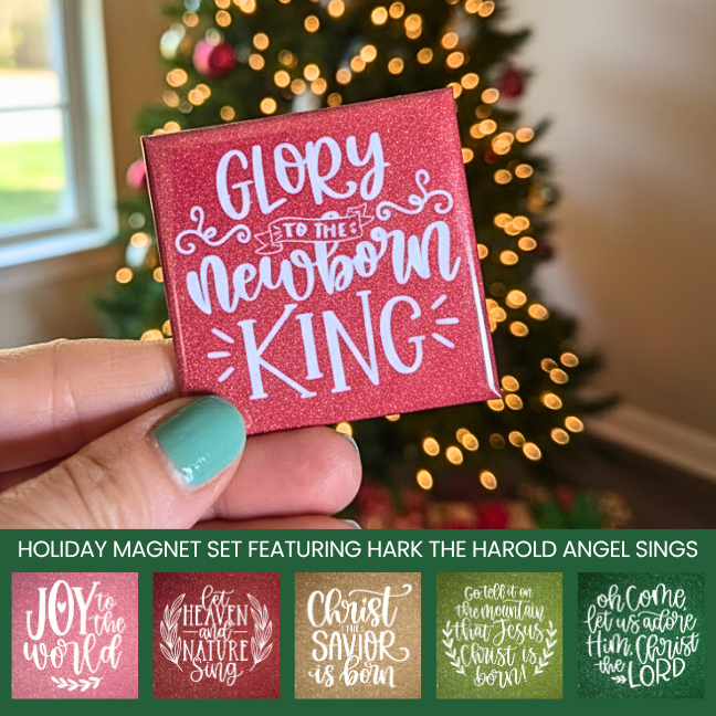 Hand holding a red magnet with 'Glory to the Newborn King' text in front of a Christmas tree.