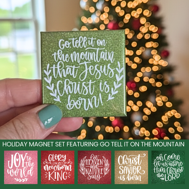 Hand holding a green holiday magnet with Christmas lyrics in front of a blurred Christmas tree.