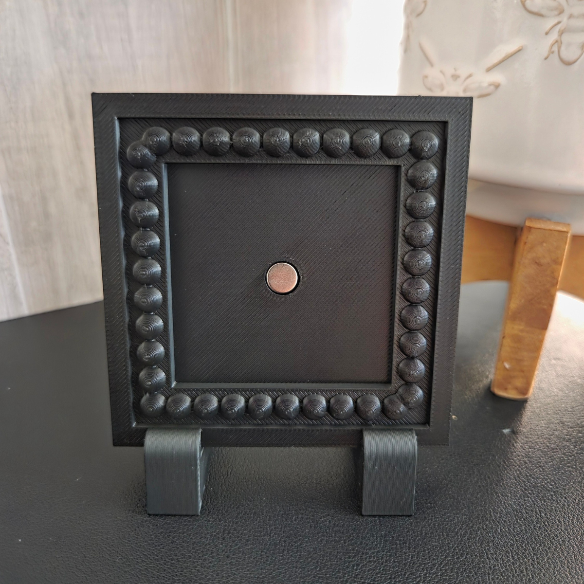 White 3D‑printed 1×1 magnetic frame with a decorative beaded border, shown standing with removable feet for tabletop display.