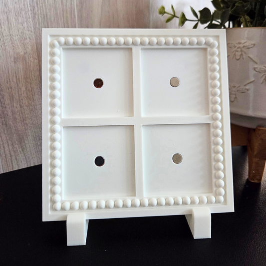 White 3D‑printed 2x2 magnetic frame with a decorative beaded border, designed to hold 4 photo magnets in portrait or landscape orientation, shown with removable feet.
