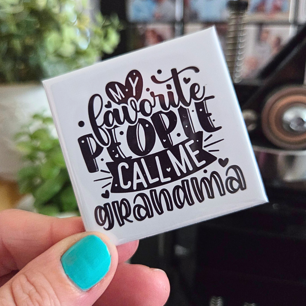 Square white card with 'Favorite people call me grandma' text held by a hand with teal nail polish.