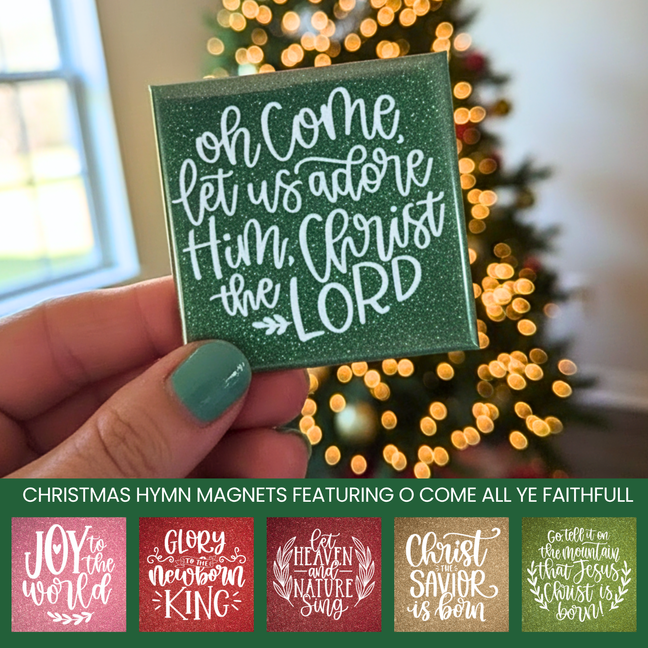 Hand holding a Christmas magnet with 'oh come, let us adore Him, Christ the Lord' text in front of a blurred Christmas tree.