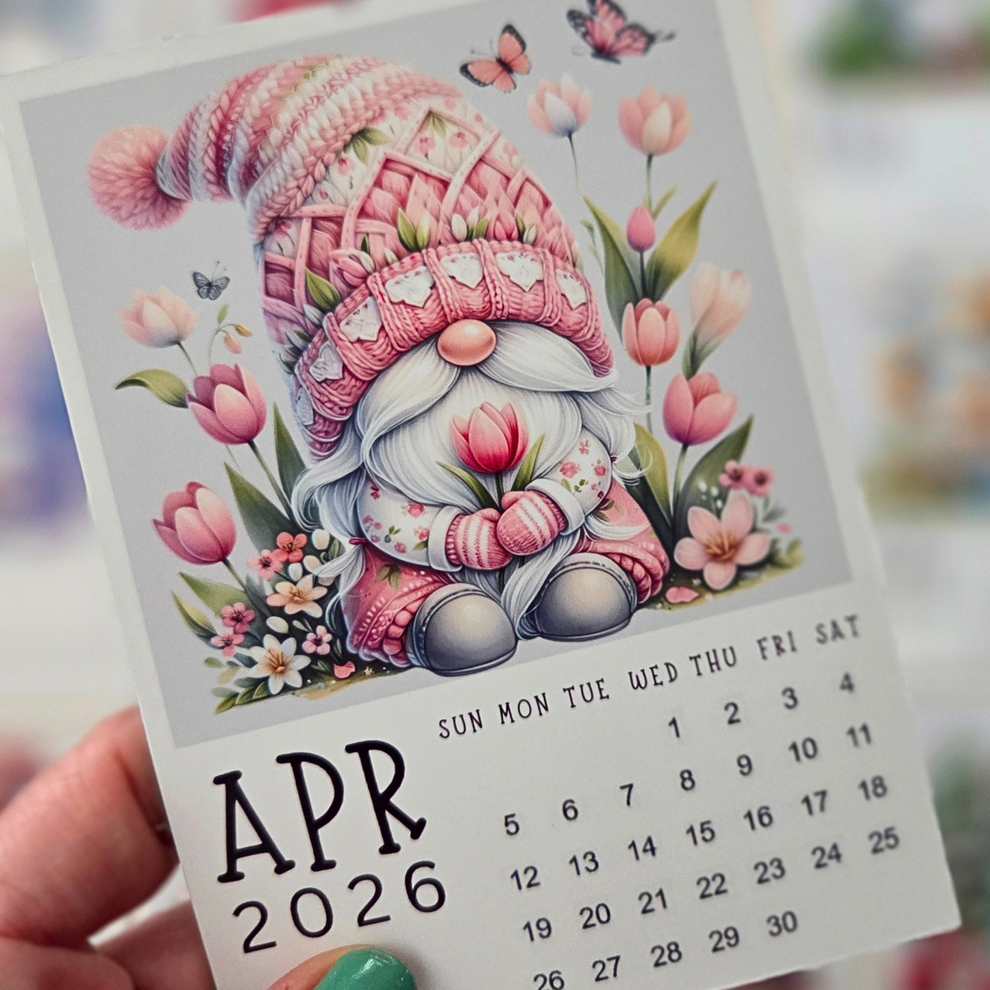 Calendar for April 2026 with a gnome illustration wearing a pink hat and holding tulips.