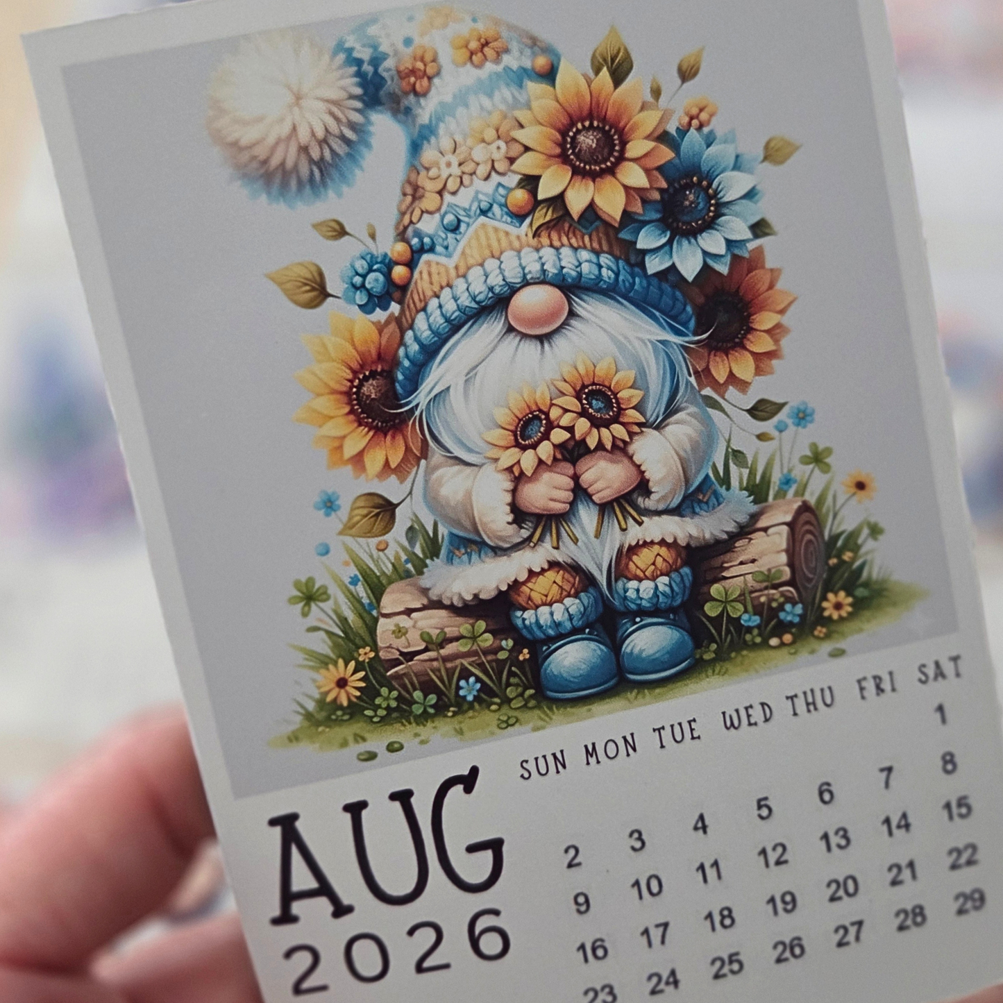Calendar for August 2026 featuring a gnome with flowers, held by a hand.