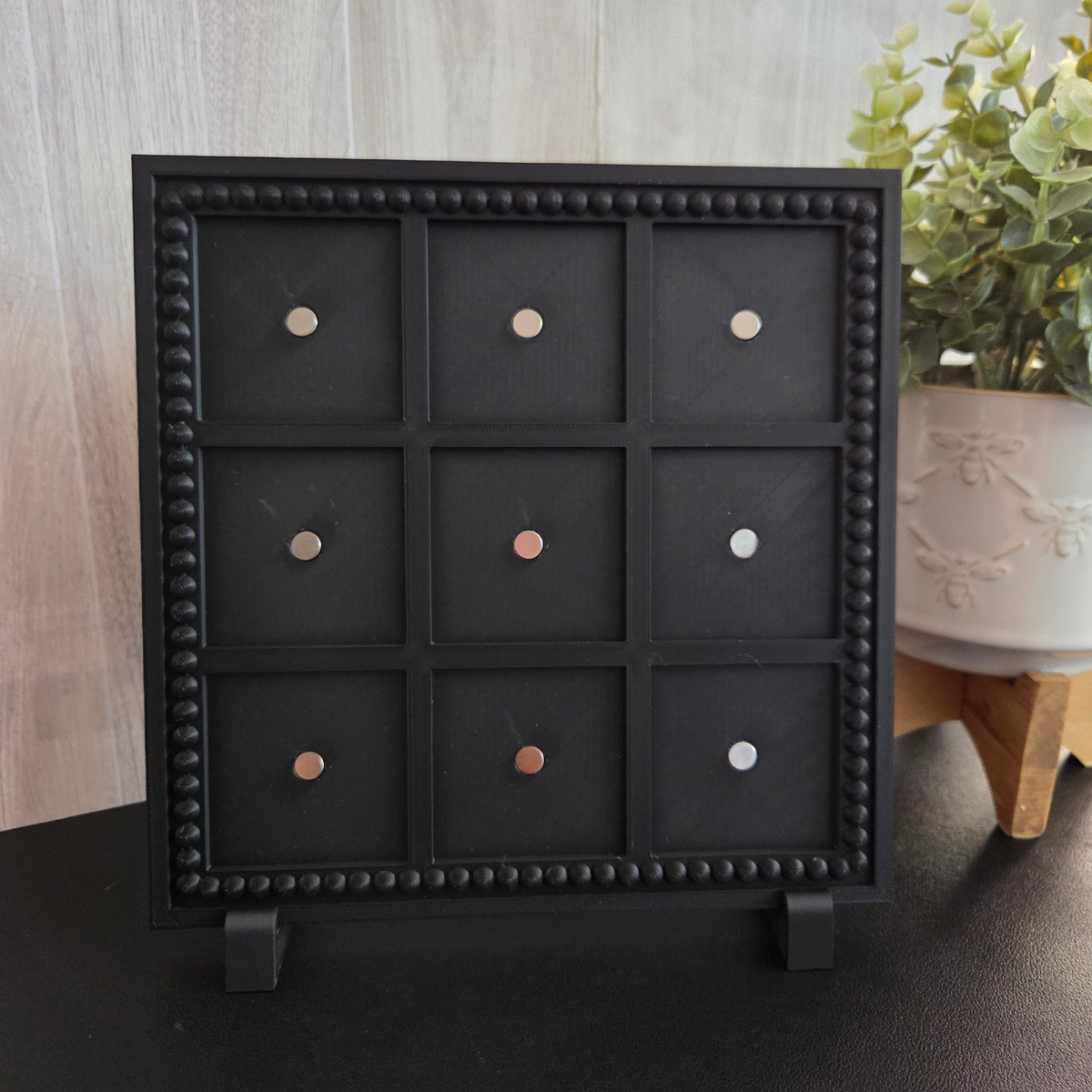 Black 3D‑printed 3×3 magnetic frame with a decorative beaded border, designed to hold nine photo magnets in a clean grid layout, shown with removable feet and clearly labeled as holding 9 photo magnets.