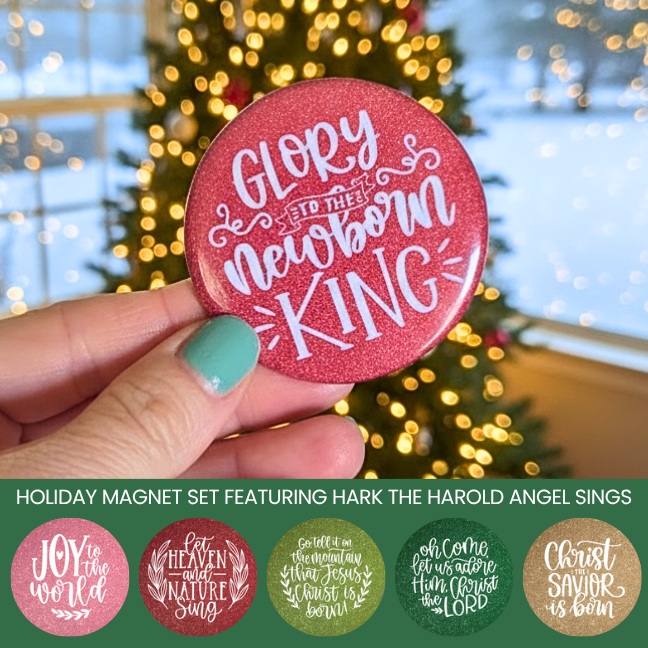 Red holiday magnet with 'Glory to the newborn king' text held in front of a Christmas tree.