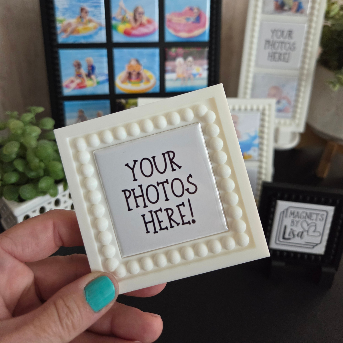Hand holding a decorative photo frame with 'Your Photos Here!' text, with more frames and a plant in the background.
