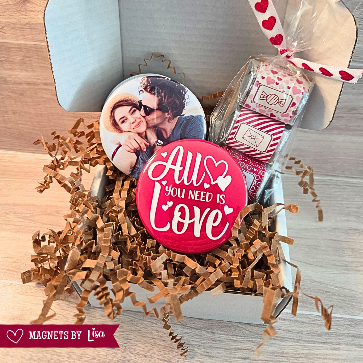 Valentine’s Day gift box with custom 2-inch round photo magnets, a All you Need is Love magnet, and a  trio of Hershey chocolate nuggets wrapped in pink and red Valentine-themed stickers.