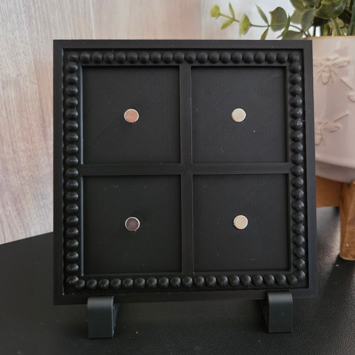 Black 3D‑printed 2x2 magnetic frame with a decorative beaded border, designed to hold 4 photo magnets in portrait or landscape orientation, shown with removable feet.