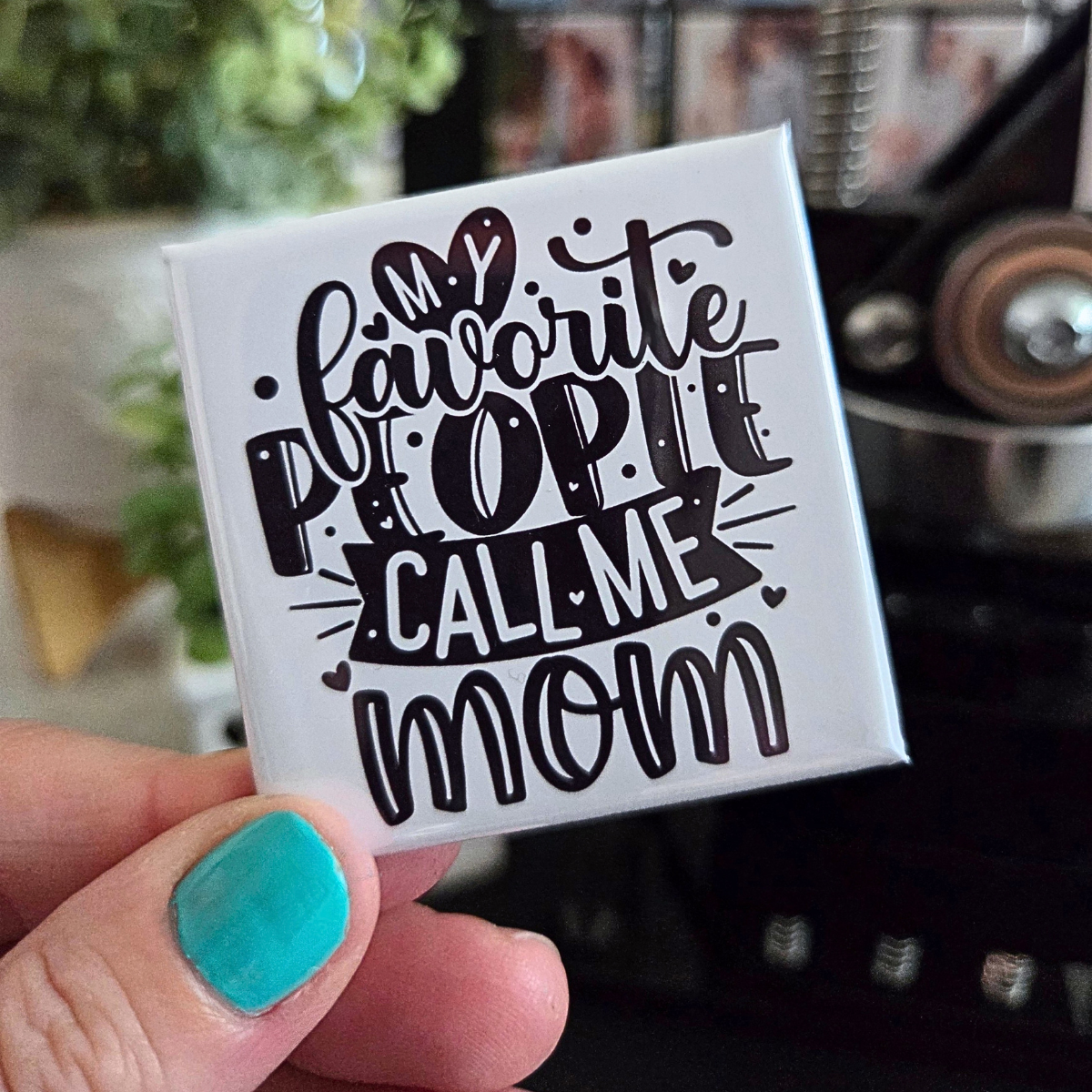 Square magnet with 'Favorite people call me mom' text held by a hand with teal nail polish.