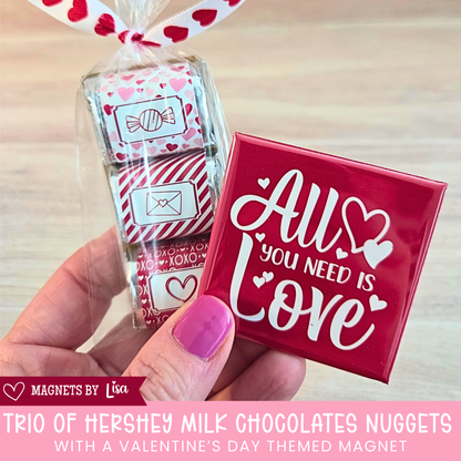 Valentine’s Day gift box with custom 2-inch square photo magnets, a All you Need is Love magnet, and a  trio of Hershey chocolate nuggets wrapped in pink and red Valentine-themed stickers.