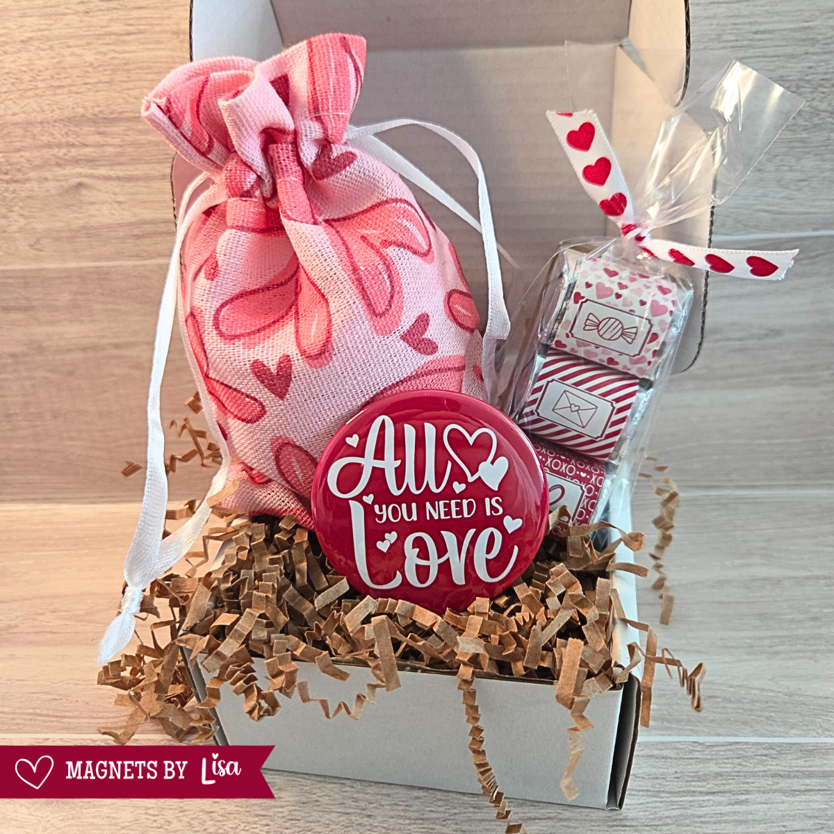 Valentine’s Day gift box with custom 2-inch round photo magnets, a All you Need is Love magnet, and a  trio of Hershey chocolate nuggets wrapped in pink and red Valentine-themed stickers.